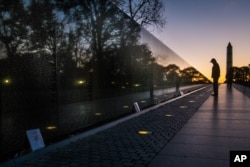FILE - A visitor pauses at the Vietnam War Memorial in Washington early in the morning on Veterans Day, Monday, Nov. 11, 2013 to look at the names inscribed on the wall. The Washington Monument is at right. (AP Photo/J. David Ake, File)