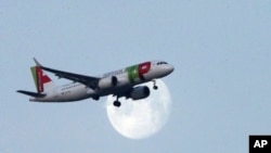 A TAP Air Portugal airplane approaches for landing in Lisbon as the moon sets, Feb. 21, 2019.