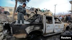 Seorang polisi Afghanistan memeriksa kendaraan yang hancur akibat serangan bom bunuh diri di gerbang markas polisi di wilayah Sarobi, sebelah timur Kabul, Afghanistan (21/2).
