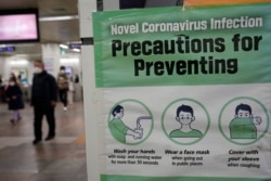 People wearing face masks pass by a poster of precautions against coronavirus at a subway station in Seoul, South Korea, Jan. 25, 2022.