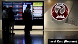 Pria berdiri di samping logo maskapai penerbangan Japan Airlines (JAL), di tengah wabah COVID-19, di Bandara Haneda di Tokyo, Jepang, 30 Oktober 2020. (Foto: REUTERS/Issei Kato)