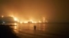 Seorang pria menyaksikan kebakaran hutan mendekati pantai Kochyli dekat desa Limni di pulau Evia, sekitar 160 kilometer utara Athena, Yunani, Jumat, 6 Agustus 2021. (AP Photo/Thodoris Nikolaou)