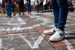 A protester stands on painted outlines of bodies representing the Colombians who disappeared during previous protests, in Bogota, July 20, 2021. (Megan Janetsky/VOA)