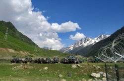 Indian army soldiers walk past their parked trucks at a makeshift transit camp before heading to Ladakh, near Baltal, southeast of Srinagar, June 16, 2020.