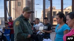 In this file photo taken on May 16, 2019 U.S. Customs and Border Protection agent checks documents of a small group of migrants, who crossed the Rio Grande from Juarez, Mexico, in El Paso, Texas.
