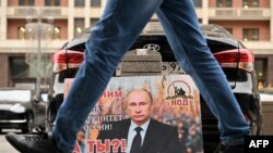 A placard featuring an image of Russian President Vladimir Putin and reading "We are with him for the sovereignty of Russia! And you?" is seen left in front of the Russian State Duma building in central Moscow.