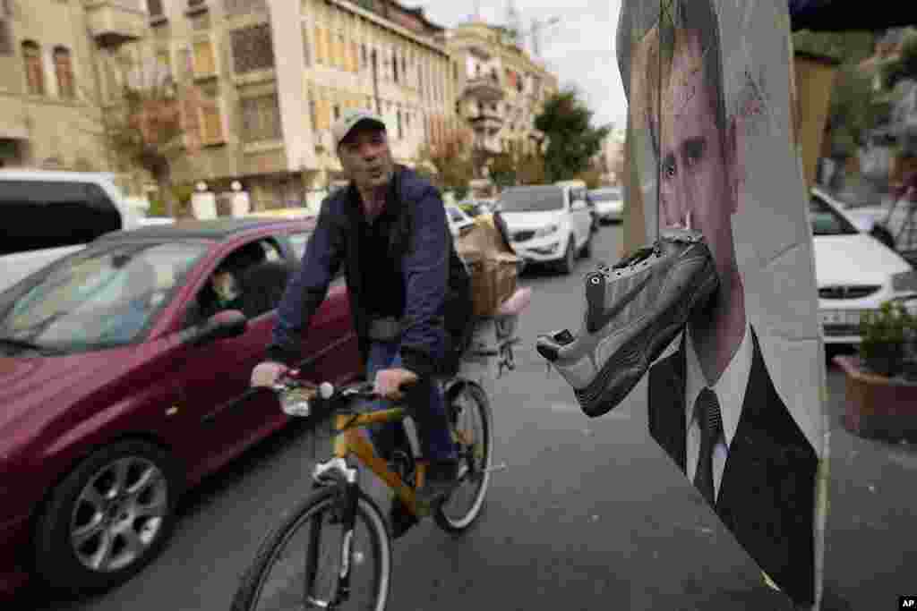 A cyclist rides past a portrait of ousted Syrian President Bashar al-Assad with a shoe attached to it as a sign of disdain, in Damascus, Syria.