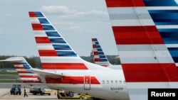 FILE - A member of a ground crew walks past American Airlines planes parked at the gate during the coronavirus outbreak at Ronald Reagan National Airport in Washington, April 5, 2020.