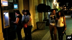 A couple passes by people using ATM machines in Monastiraki in Athens, early Monday, June 29, 2015.