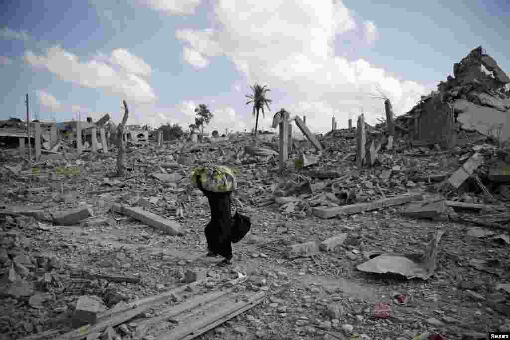 A Palestinian woman carries belongings while walking over the rubble of buildings destroyed by what police said were Israeli air strikes and shelling in Khuzaa, east of Khan Younis, in the southern Gaza Strip.