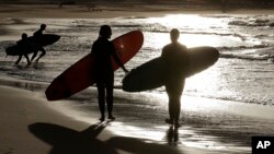 In this April 28, 2020, file photo, surfers walk along Bondi Beach in Sydney as coranavirus pandemic restrictions are eased. U.S. biotechnology company Novavax began injecting a coronavirus vaccine candidate into people in Australia.