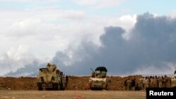 Iraqi soldiers gather near vehicles as smoke rises from oil wells in the Ajil field east of Tikrit in the Salahuddin province that were set on fire by Islamic State militants, March 4, 2015. 