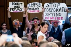 Members of the audience hold up signs and wear sunglasses that read "Stop Spying" before CEO Mark Zuckerberg arrives to testify before a joint hearing of two Senate committees on Capitol Hill in Washington, April 10, 2018.
