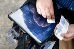 Joseph Ortiz, a contact tracer with New York City's Health + Hospitals battling the coronavirus pandemic, disinfects his tablet after leaving a potential patient's home Thursday, Aug. 6, 2020, in New York.