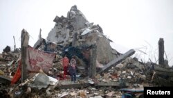 Palestinian children take cover from the rain as they stand atop the ruins of a house, which witnesses said was destroyed by Israeli shelling during the most recent conflict between Israel and Hamas, on a rainy day in the east of Khan Younis in the southe