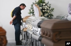 Roberto D'marchi gazes into the casket containing the remains of his cousin of Nilson Folle Jr., a victim of the Colombian air tragedy, in the parking garage of the San Vicente funeral home in Medellin, Colombia, Dec. 1, 2016. Because of the large number of casualties, the funeral home had to place the coffins in its parking garage. Forensic authorities say they have managed to identify a majority of the victims of Monday's crash and hope to finish their work Thursday. Folle Jr. was a member of the Chapecoense soccer club's board of directors.