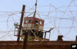 FILE - An Egyptian soldier on a watchtower looks through binoculars as bulldozers work on creating a buffer zone along the Egyptian border with the Gaza strip, in Rafah, June 28, 2017.