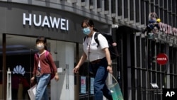 Residents wearing face masks to protect against the coronavirus walk past a Huawei retail store in Beijing on Monday, May 18, 2020. China's commerce ministry says it will take "all necessary measures" in response to new U.S. restrictions on Chinese…