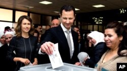 Syrian President Bashar al-Assad casts his ballot in parliamentary elections as wife Alma, left, observes, in Damascus, April 13, 2016. The photo was posted on the official Facebook page of the Syrian Presidency. 