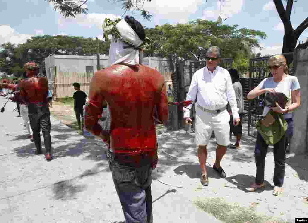 Tourists watch as penitents, bloodied after self-flagellation, walk during a Good Friday crucifixion re-enactment in San Pedro Cutud, Pampanga province, Philippines, March 29, 2013.