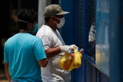 A health worker, right, stands behind a gate at an athletic dorm facility being used to house Guatemalans deported from the U.S., as a man brings food to the deportees in Guatemala City, April 17, 2020.