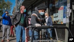 FILE - A masked grocery store worker in Brooklyn's Sunset Park, a neighborhood with one of the city's largest Mexican and Hispanic community, organizes shopping carts May 5, 2020, in New York.