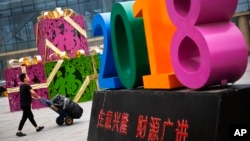 Seorang pria mendorong gerobak barangnya melewati dekorasi yang melambangkan semangat untuk menggapai "Kesuksesan dan Ledakan Bisnis Tahun 2018" di luar pusat pakaian eceran dan grosir di Beijing, China, 9 Juli 2018. (Foto: dok).