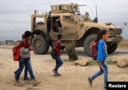 FILE - Syrian schoolchildren walk as U.S. troops patrol near the Turkish border in Hasakah, Syria, Nov. 4, 2018.