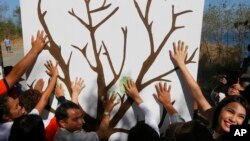 Para aktivis lingkungan membuat simbol dengan tangan mereka di atas kertas bergambar pohon dalam acara pembersihan wilayah pantai di Freedom Island, daerah sub-urban kota Las Pians, selatan Manila, Filipina untuk menandai peringatan Hari Bumi (22/4). 