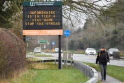 A person walks past a roadside public health information sign, amidst the spread of the coronavirus disease (COVID-19) pandemic, near Oxford, Britain, Dec. 28, 2020.