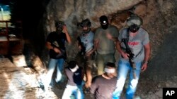 Dalam foto yang dirilis Kepolisian Israel, pihak keamanan Israel berdiri di samping buron Palestina, Zakaria Zubeidi (kiri) dan Mohammed Aradeh, yang ditutup mata dan diborgol setelah ditangkap di Kota Umm al-Ghanam, di utara Israel, Sabtu, 11 September 2021. (Foto: AP)
