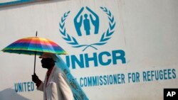 A Congolese man carries an umbrella decorated with a United Nations flag as Muslim and Christian refugees protest together outside the head office of the United Nations refugee agency in Bangui, Central African Republic, Jan. 6, 2014.