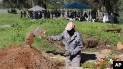 A gravedigger works in the COVID-19 section of the Maitland Cemetery in Cape Town, South Africa, July 15, 2020 as a burial takes place in the background. 