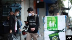 FILE - People walk by a poster reading in Vietnamese "Fighting COVID-19" in Hanoi, Vietnam, Apr. 23, 2020. Business activities are resuming in Vietnam as the country lifts the nationwide lockdown to contain the spread of COVID-19.
