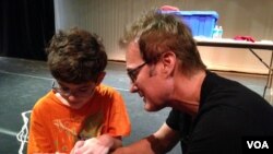 Magician Kevin Spencer teaches Liam Shannon a magic trick. (VOA/ J.Taboh)