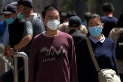 People wearing protective face masks to help curb the spread of the new coronavirus walk in downtown Beijing, Monday, May 18, 2020.