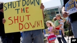 As the federal government shutdown continues, Tory Anderson, right, with her kids Audrey, 7, and Kai, 3, of Goodyear, Ariz., join others as they rally for the Alliance of Retired Americans to end the shutdown, Oct. 9, 2013.