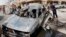 People inspect a car destroyed in a car bomb attack close to one of the main gates to the heavily-fortified Green Zone in Baghdad, Iraq, March 19, 2013. 