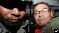 FILE - In this Oct. 7, 2015, file photo, Hong Sok Hour, right, a senator from the main opposition Cambodia National Rescue Party, is escorted by riot police officers at Phnom Penh Municipal Court in Phnom Penh, Cambodia. Phnom Penh Municipal Court on Monday, Nov. 7, 2016, sentenced Hong Sok Hour to seven years in prison over comments he posted on Facebook criticizing a 36-year-old border agreement with neighboring Vietnam. The court judge found him guilty of falsifying public documents, using fake documents and inciting chaos. (AP Photo/Heng Sinith, File)