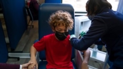 FILE - Max Cuevas, 12, holds his mother's hand as he receives the Pfizer COVID-19 vaccine from nurse practitioner Nicole Noche at Families Together of Orange County in Tustin, California, May 13, 2021.