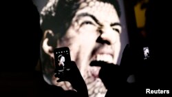 People use mobile devices to take pictures of an advertising placard showing Uruguay's striker Luis Suarez flashing his teeth, Copacabana beach, Rio de Janeiro, June 26, 2014.