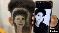 Gurwinder Singh Sidhu, 31, a barber, displays a photo of Michael Jackson next to a customer after he made a hair tattoo of the pop star in the customer's hair inside his shop. (REUTERS/Sunil Kataria)