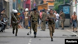 Sri Lankan police clear the area while Special Task Force Bomb Squad officers inspect the site of an exploded van near a church that was attacked yesterday in Colombo, April 22, 2019. 