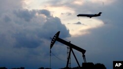 21일 미국 오클라호마주 오클라호마시티에 해가 지는 가운데 석유를 뽑아 올리는 '펌프잭' 위로 항공기가 착륙하고 있다. 신종 코로나바이러스 감염증(COVID-19)의 여파로 항공편 결항과 공장 가동 중단 등 원유 수요가 줄어들면서 유가가 계속 하락하고 있다.
