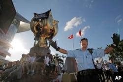 FILE - A policeman tries to stop members of the Demosisto political party and other pro-democracy activists from climbing a giant flower statue given to Hong Kong from Beijing in 1997 in Golden Bauhinia Square, Hong Kong, June 28, 2017.