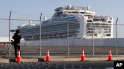 A photographer takes photos near the quarantined Diamond Princess cruise ship anchored at a port in Yokohama, near Tokyo, Friday, Feb. 21, 2020. Passengers tested negative for COVID-19 started disembarking since Wednesday. (AP Photo/Eugene Hoshiko)