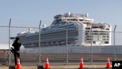 A photographer takes photos near the quarantined Diamond Princess cruise ship anchored at a port in Yokohama, near Tokyo, Friday, Feb. 21, 2020. Passengers tested negative for COVID-19 started disembarking since Wednesday. (AP Photo/Eugene Hoshiko)