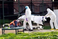 បុគ្គលិកពេទ្យ​កំពុង​ដឹក​សព​ចេញ​ពី​កុង​តឺន័រ​សម្រាប់​បង្កក នៅ​ឯ​មន្ទីរ​ពេទ្យ Kingsbrook Jewish Medical Center កាល​ពី​ថ្ងៃ​ទី ២៨ មេសា ២០២០ នៅ​ទីក្រុង​ញូវយ៉ក។