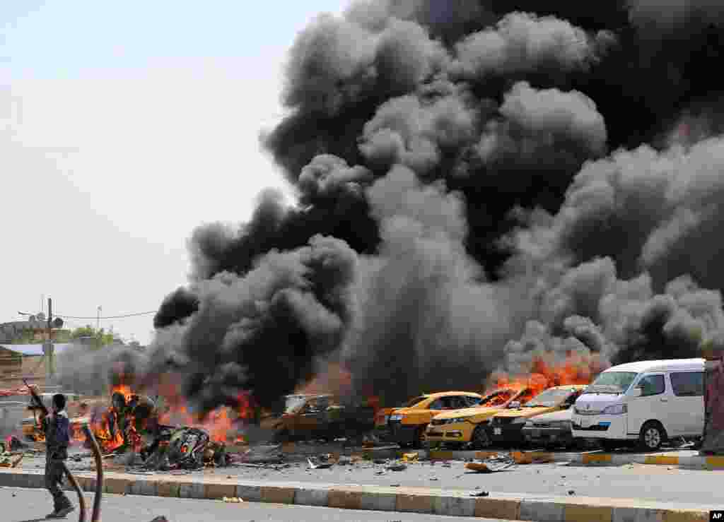 A police officer stands near burning vehicles moments after one in a series of bombs hit the Shi'ite stronghold of Sadr City, in Baghdad, May 13, 2014. 