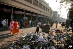 People cover their noses as they walk past trash strewn on a street, in Varanasi, India, March 22, 2019.